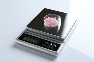 Photo of Laboratory scale with Petri dish of sample on white background, closeup