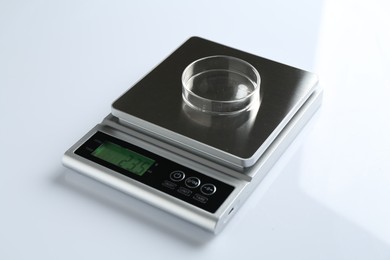 Photo of Laboratory scale with Petri dish on white background, closeup