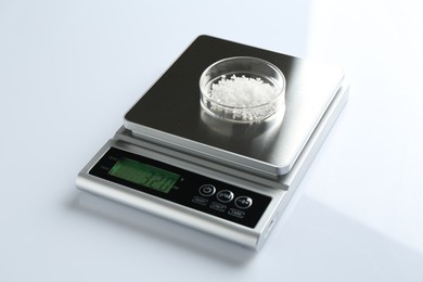 Photo of Laboratory scale with Petri dish of sample on white background, closeup