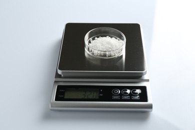 Photo of Laboratory scale with Petri dish of sample on white background, closeup