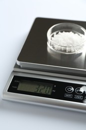 Photo of Laboratory scale with Petri dish of sample on white background, closeup