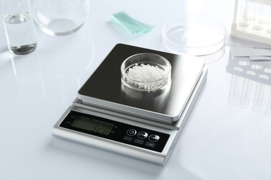 Photo of Scale with Petri dish of sample and other laboratory equipment on white background, closeup