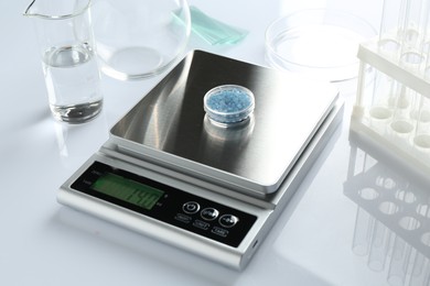 Photo of Scale with Petri dish of sample and other laboratory equipment on white background, closeup