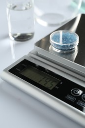 Photo of Laboratory scale with Petri dish of sample on white background, closeup