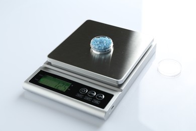 Photo of Laboratory scale with Petri dish of sample on white background, closeup