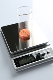 Photo of Laboratory scale with beaker of sample on white background, closeup