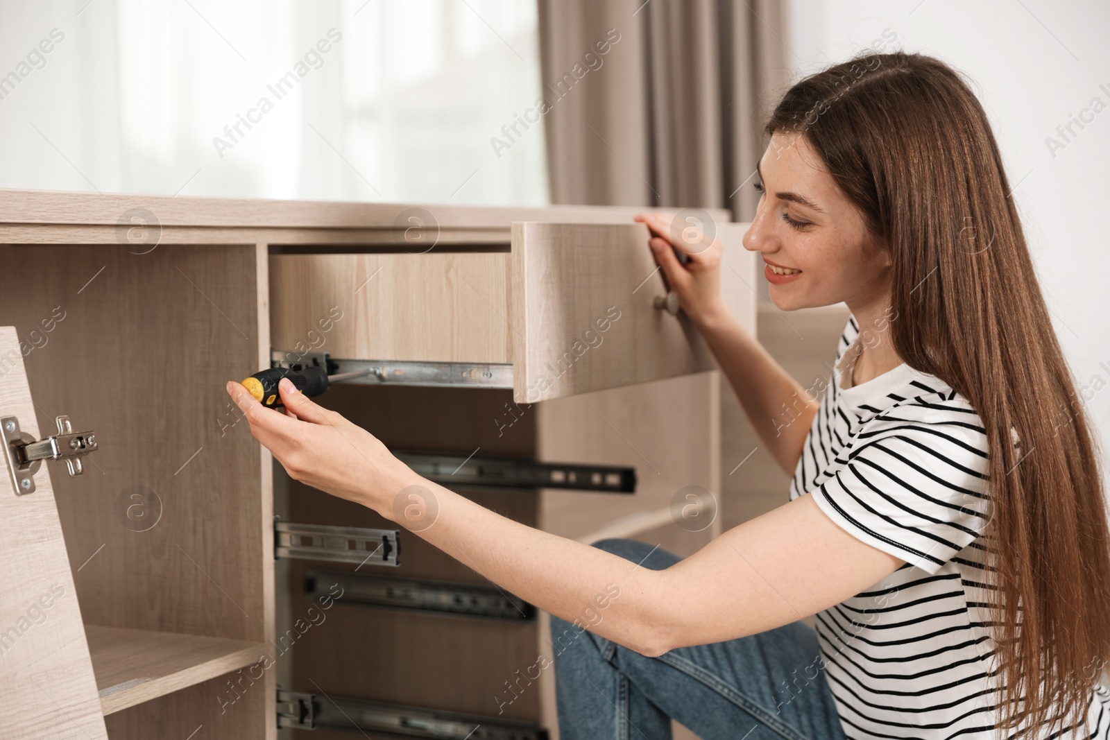 Smiling woman assembling furniture with screwdriver at home Photo of Smiling woman assembling furniture with screwdriver at home