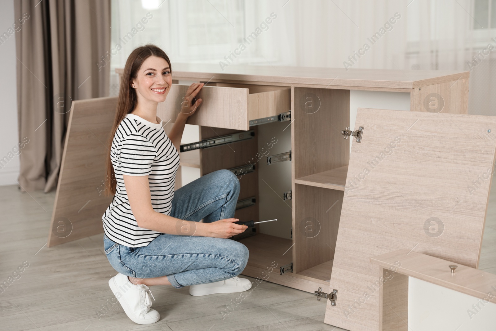 Smiling woman assembling furniture with screwdriver at home Photo of Smiling woman assembling furniture with screwdriver at home