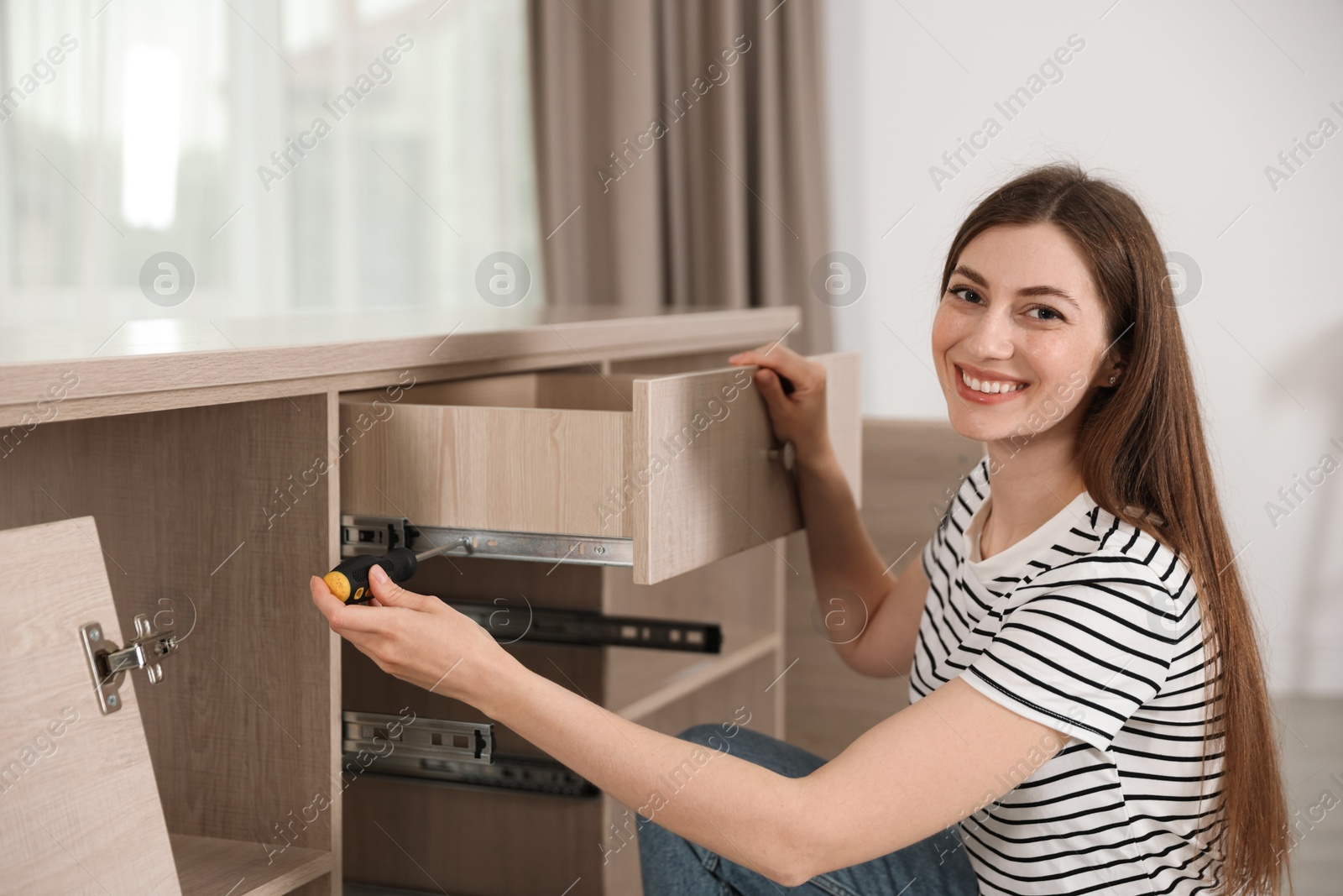 Smiling woman assembling furniture with screwdriver at home Photo of Smiling woman assembling furniture with screwdriver at home