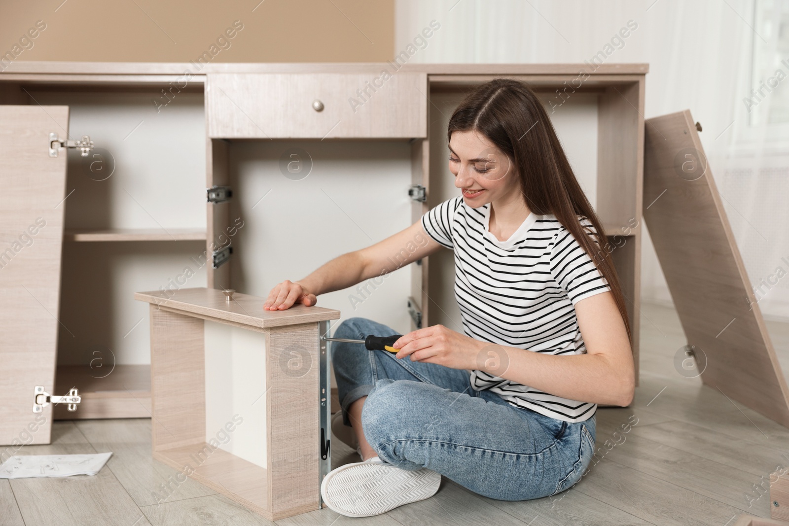 Smiling woman assembling furniture with screwdriver on floor at home Photo of Smiling woman assembling furniture with screwdriver on floor at home