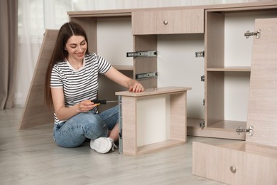 Photo of Smiling woman assembling furniture with screwdriver on floor at home