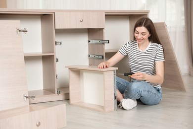 Photo of Smiling woman assembling furniture with screwdriver on floor at home