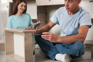 Photo of Couple assembling furniture with screwdriver on floor at home, selective focus