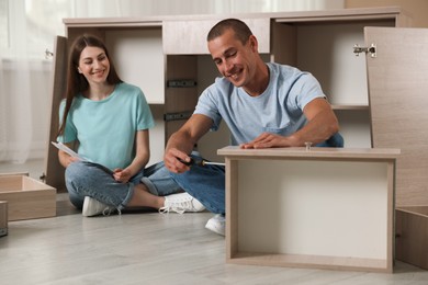 Photo of Happy couple assembling furniture on floor at home