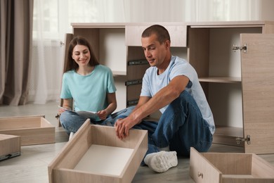 Photo of Happy couple assembling furniture on floor at home