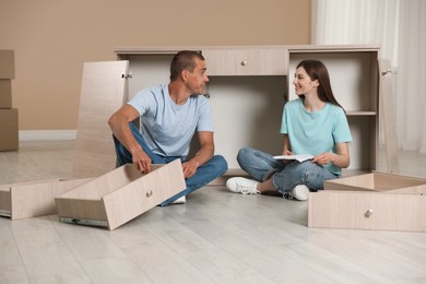 Photo of Happy couple assembling furniture on floor at home