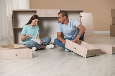 Photo of Happy couple with manual assembling furniture on floor at home