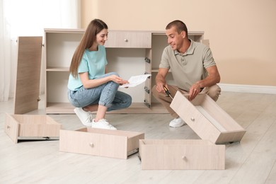 Photo of Happy couple with manual assembling furniture on floor at home