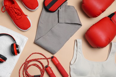 Photo of Sportswear, gloves, skipping rope, headphones and towel on beige background, flat lay
