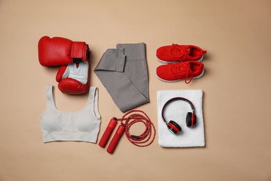 Photo of Sportswear, gloves, skipping rope, headphones and towel on beige background, flat lay