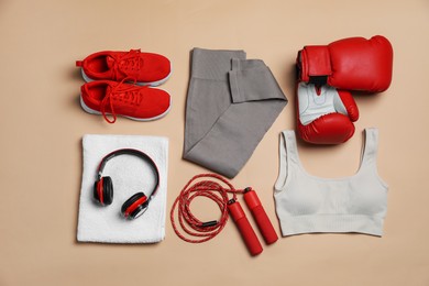 Photo of Sportswear, gloves, skipping rope, headphones and towel on beige background, flat lay