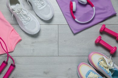 Photo of Sportswear, sneakers, skipping rope, headphones and dumbbells on floor, flat lay. Space for text