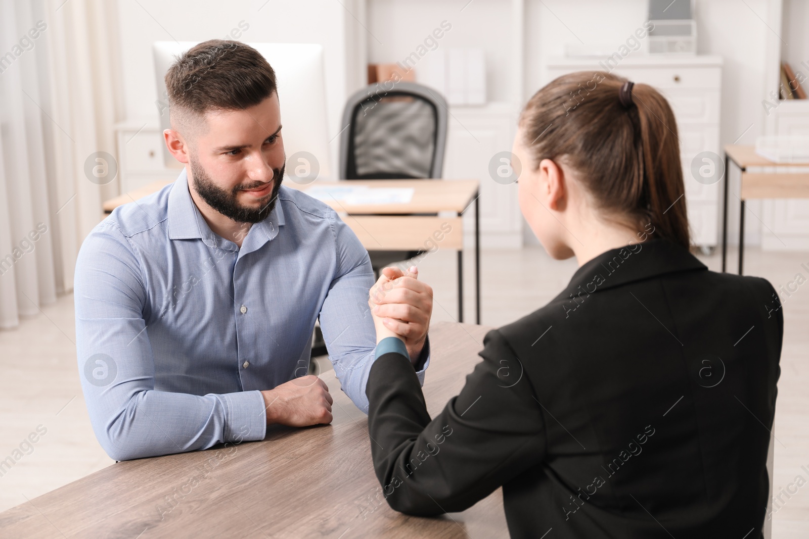 Businesspeople arm wrestling at wooden table in office Photo of Businesspeople arm wrestling at wooden table in office