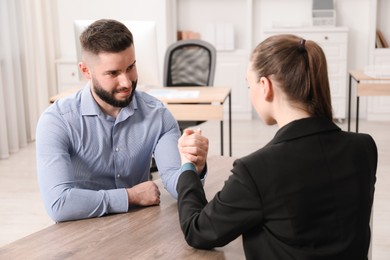 Photo of Businesspeople arm wrestling at wooden table in office