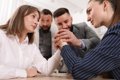 Photo of Businesswomen arm wrestling at wooden table in office, low angle view