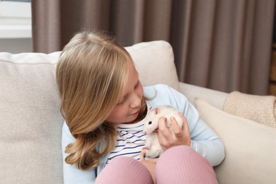 Photo of Little girl with cute white rat on sofa at home