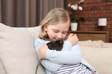 Photo of Little girl with cute black rat on sofa at home