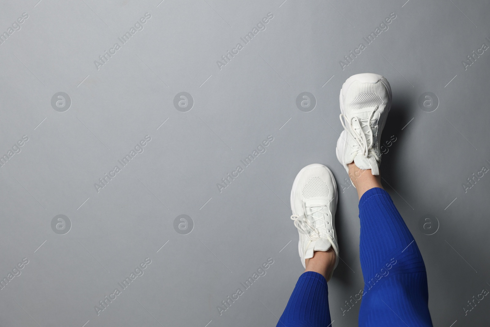 Woman in white sneakers on gray background, top view. Space for text Photo of Woman in white sneakers on gray background, top view. Space for text
