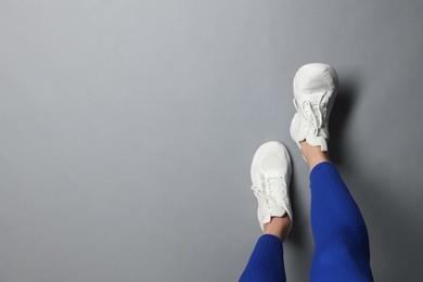 Photo of Woman in white sneakers on gray background, top view. Space for text