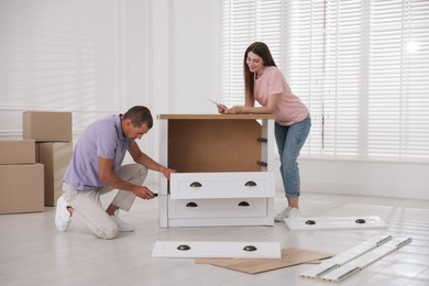 Photo of Happy couple with manual assembling furniture on floor at home