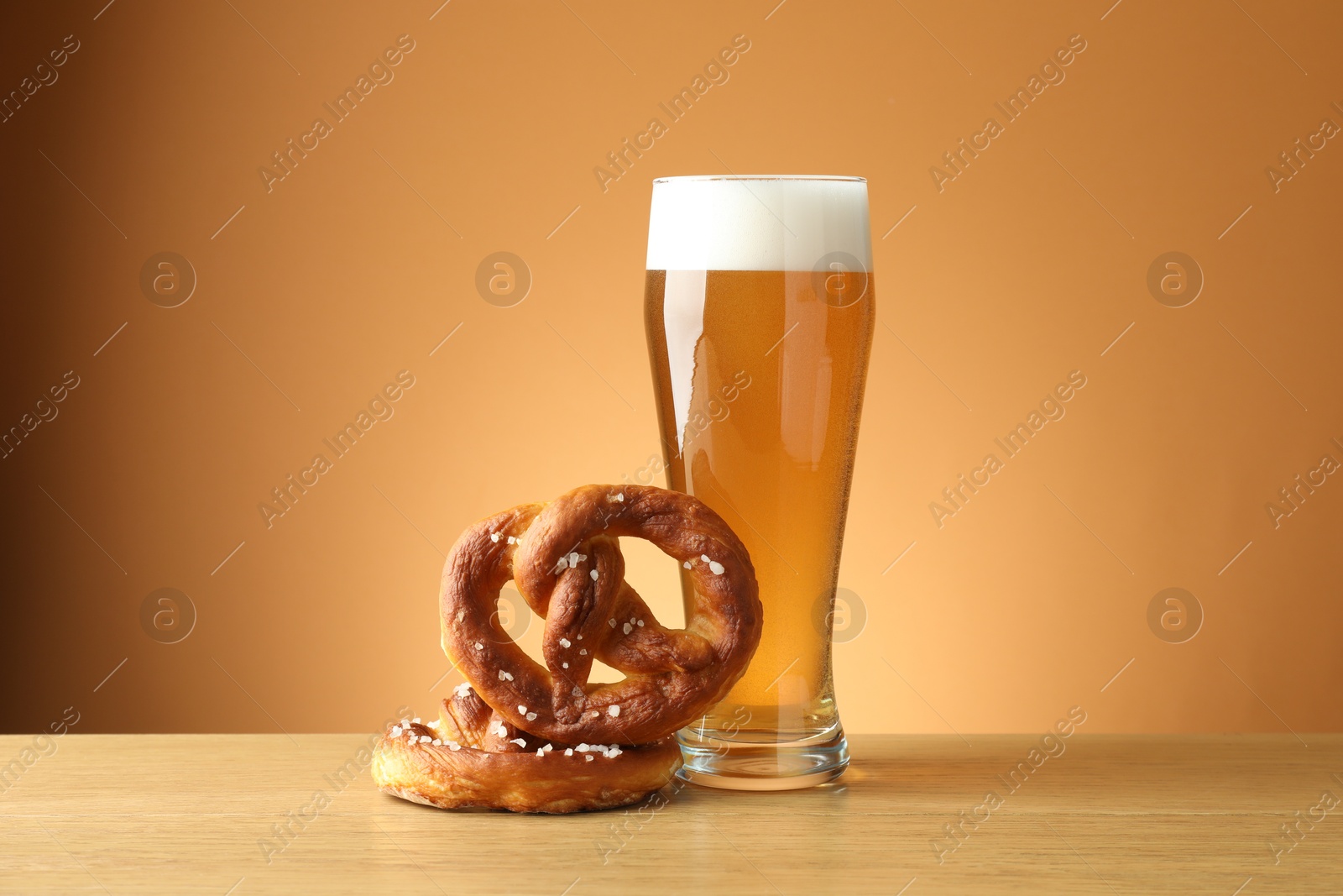 Tasty pretzels and glass of beer on wooden table against beige gradient background, closeup Photo of Tasty pretzels and glass of beer on wooden table against beige gradient background, closeup