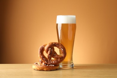 Photo of Tasty pretzels and glass of beer on wooden table against beige gradient background, closeup