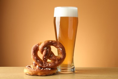 Photo of Tasty pretzels and glass of beer on wooden table against beige gradient background, closeup