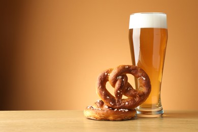 Photo of Tasty pretzels and glass of beer on wooden table against beige gradient background, closeup. Space for text