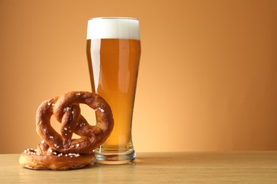 Photo of Tasty pretzels and glass of beer on wooden table against beige gradient background, closeup. Space for text