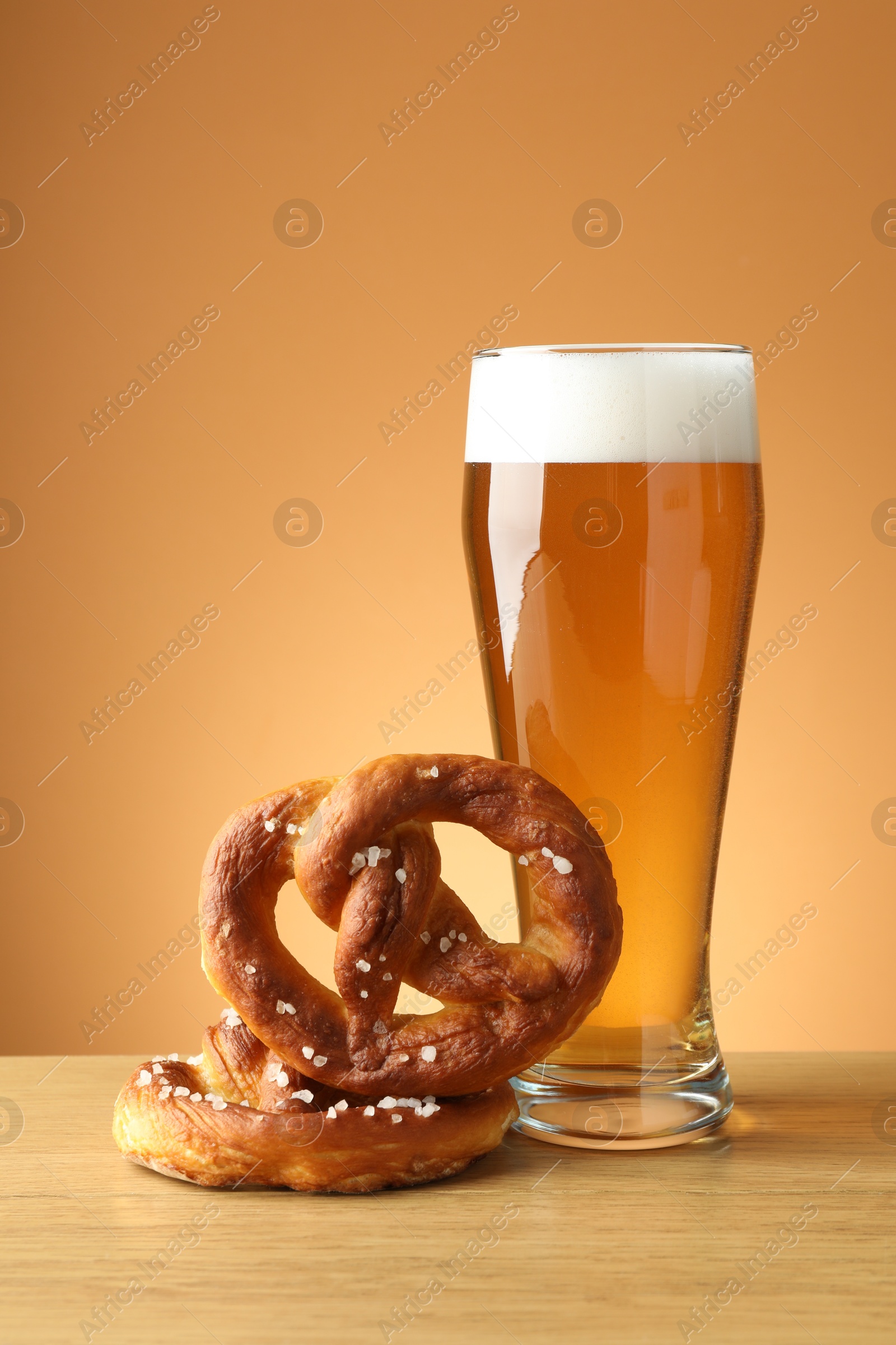 Tasty pretzels and glass of beer on wooden table against beige gradient background, closeup Photo of Tasty pretzels and glass of beer on wooden table against beige gradient background, closeup