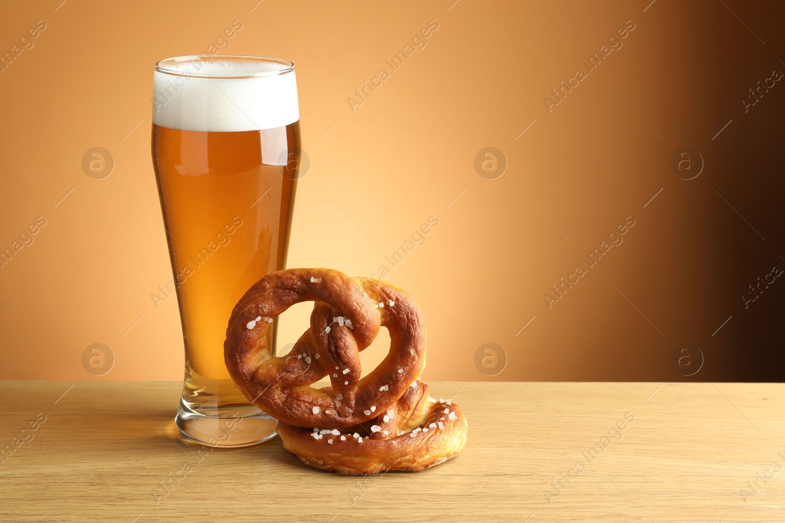 Tasty pretzels and glass of beer on wooden table against beige gradient background, closeup. Space for text Photo of Tasty pretzels and glass of beer on wooden table against beige gradient background, closeup. Space for text