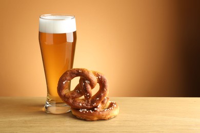 Photo of Tasty pretzels and glass of beer on wooden table against beige gradient background, closeup. Space for text