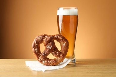 Photo of Tasty pretzel and glass of beer on wooden table against beige gradient background, closeup