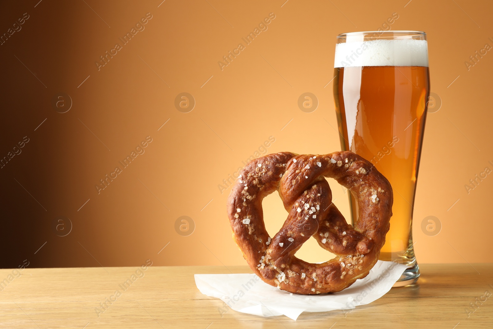 Tasty pretzel and glass of beer on wooden table against beige gradient background, closeup. Space for text Photo of Tasty pretzel and glass of beer on wooden table against beige gradient background, closeup. Space for text