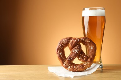 Photo of Tasty pretzel and glass of beer on wooden table against beige gradient background, closeup. Space for text
