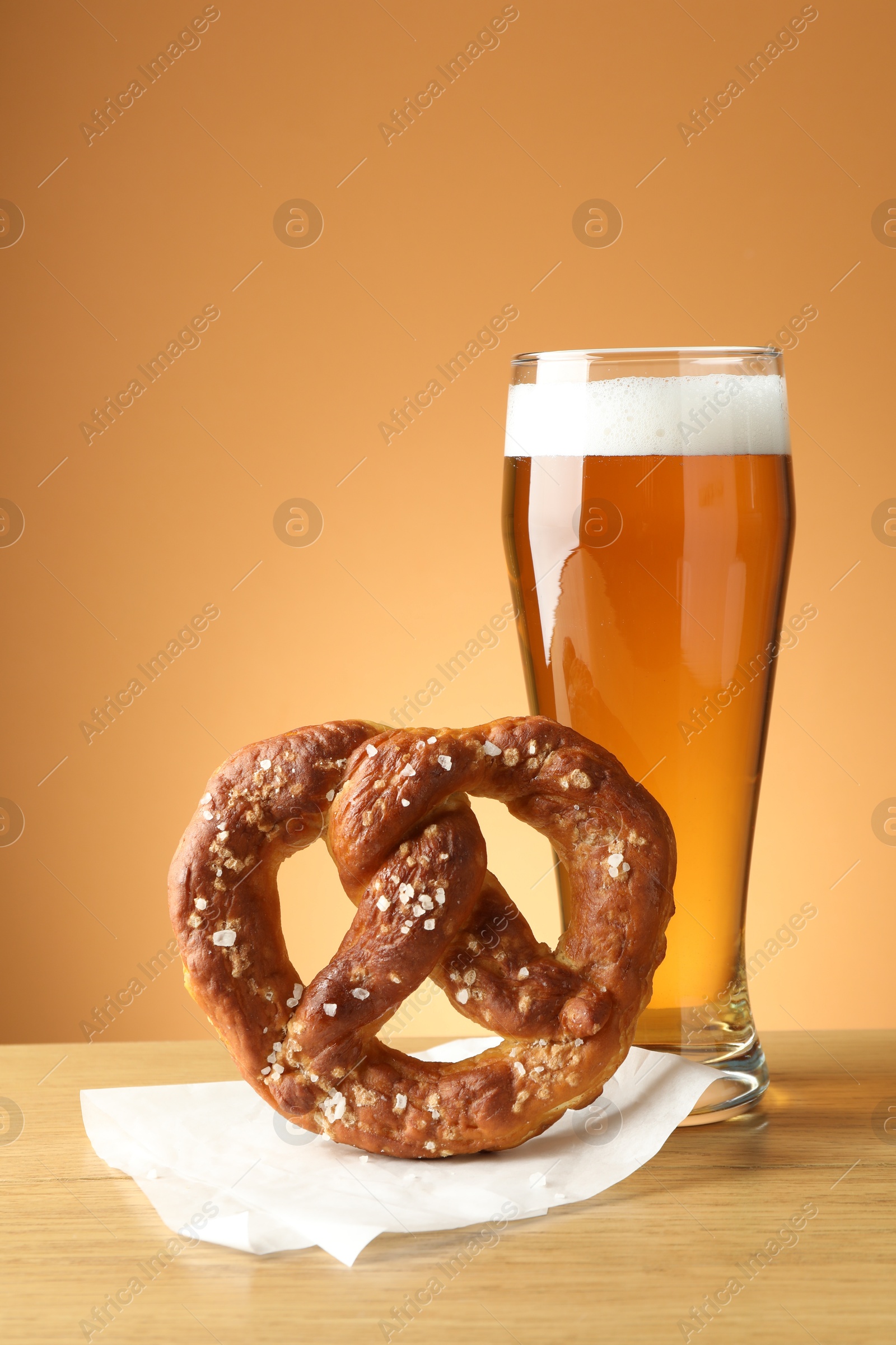 Tasty pretzel and glass of beer on wooden table against beige gradient background, closeup Photo of Tasty pretzel and glass of beer on wooden table against beige gradient background, closeup
