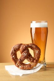 Photo of Tasty pretzel and glass of beer on wooden table against beige gradient background, closeup