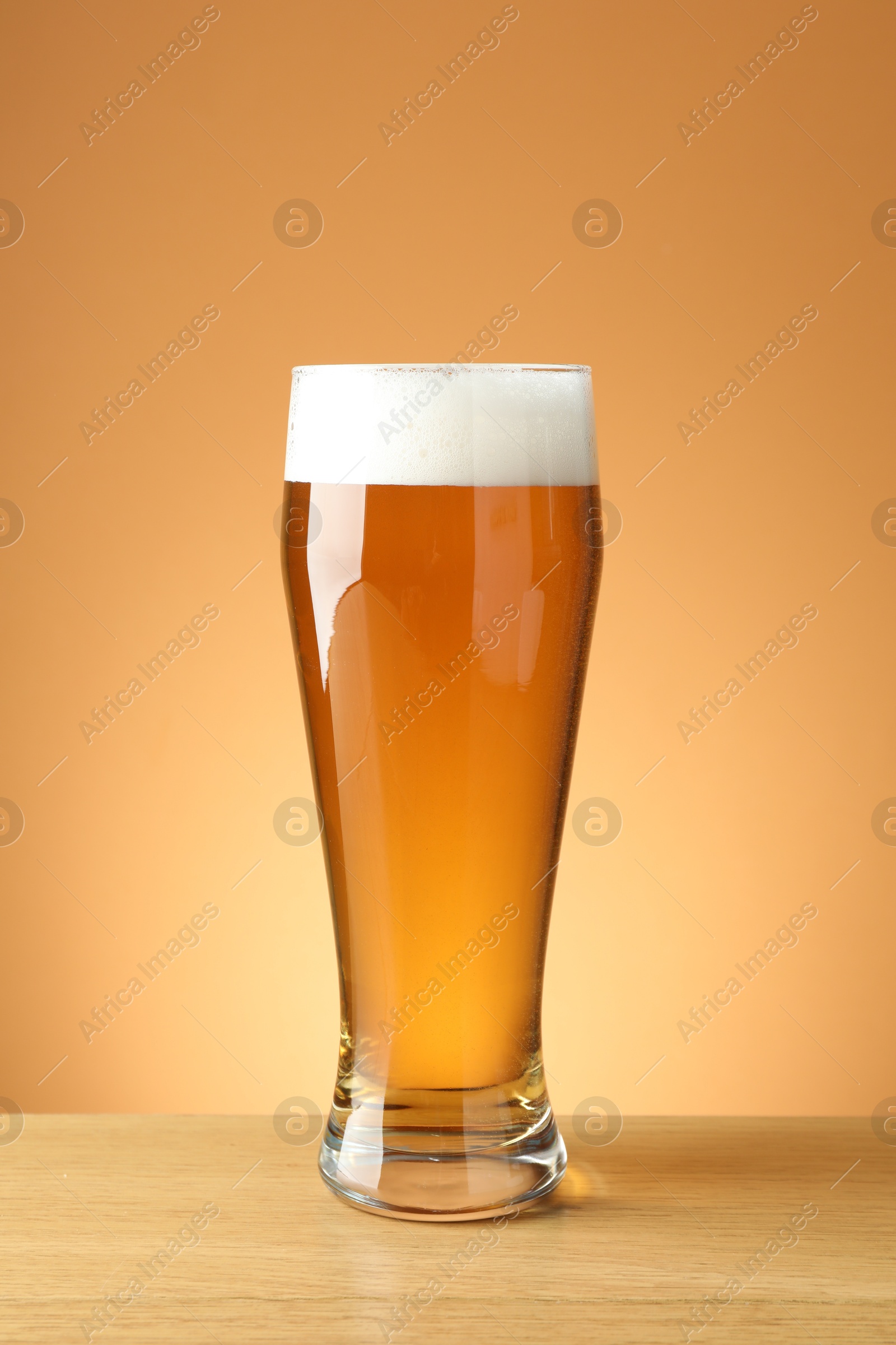 Fresh beer in glass on wooden table against beige gradient background, closeup Photo of Fresh beer in glass on wooden table against beige gradient background, closeup