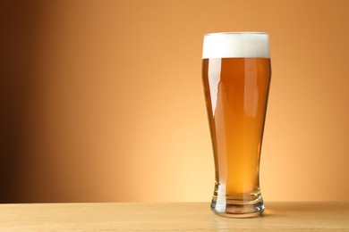 Photo of Fresh beer in glass on wooden table against beige gradient background, closeup. Space for text