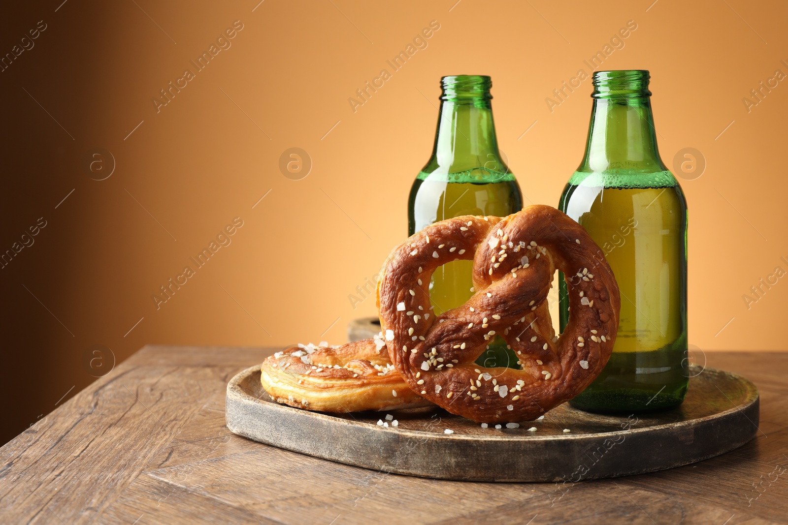 Photo of Tasty pretzels and bottles of beer on wooden table against beige gradient background, closeup. Space for text